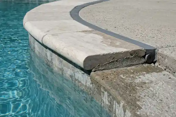 Close-up detail of bullnose pool coping stone set over a mortar bed and waterline tile with a gray elastomeric perimeter expansion joint against the concrete deck